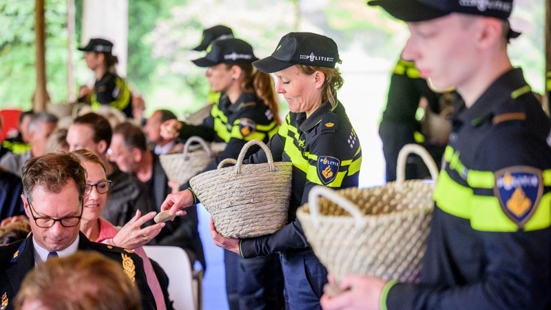 Politieaspiranten delen kiezelstenen uit aan de genodigden bij de opening van De Spiegelvijver.