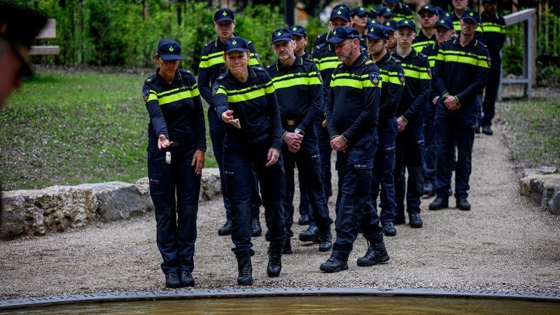 Politiemensen werpen symbolisch een kiezelsteen in De Spiegelvijver. Op de stenen staan persoonlijke boodschappen voor de overledenen.